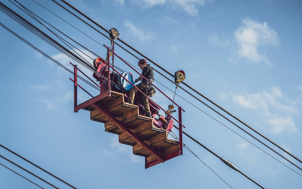 Arbeiterplattform mit Technikern um das neue Stahlseil der Gondelbahn zu montieren.