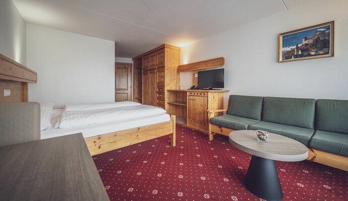 Double room with carpeted floor, sofa bed and side table | © Davos Klosters Mountains