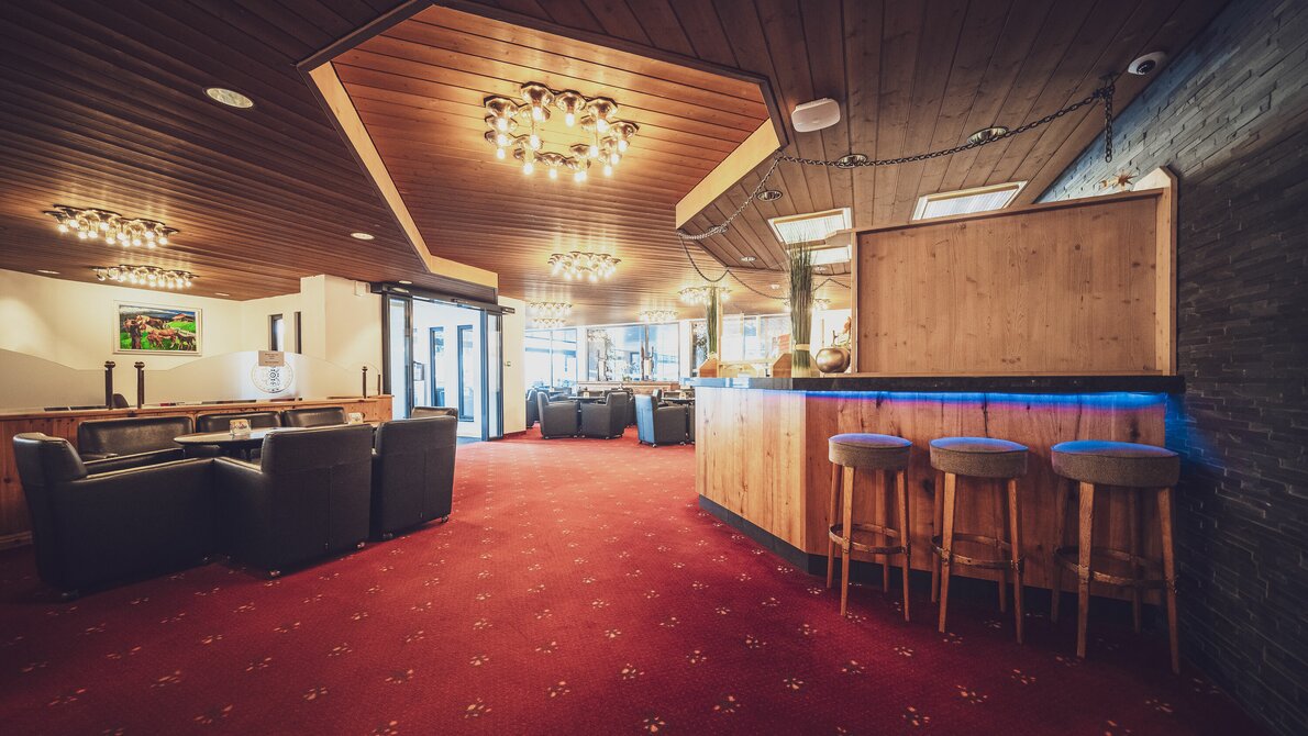 Hotel lobby incl. bar with bar seats, club tables and lounge chairs, red carpeting | © Davos Klosters Mountains 