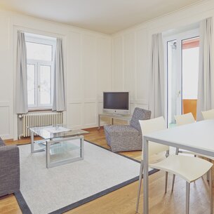 Bright apartment with windows, curtains, lounge chair, coffee table and dining table with chairs  | © Davos Klosters Mountains 